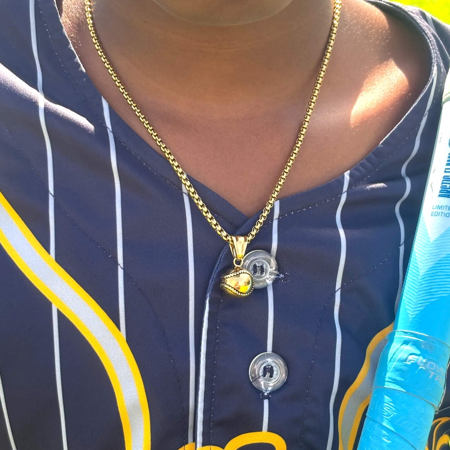 Gold plated 3D baseball pendant on a 3mm box chain necklace worn over a striped baseball jersey