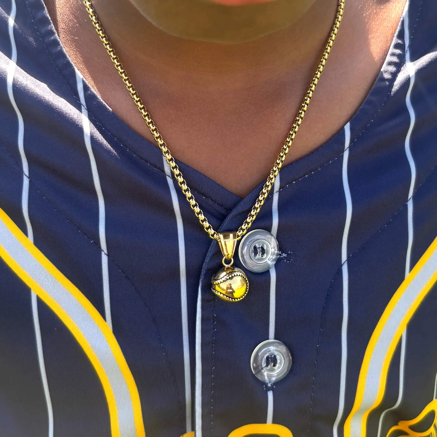 Gold 3D baseball pendant on a gold box chain necklace worn with a navy and yellow sports jersey
