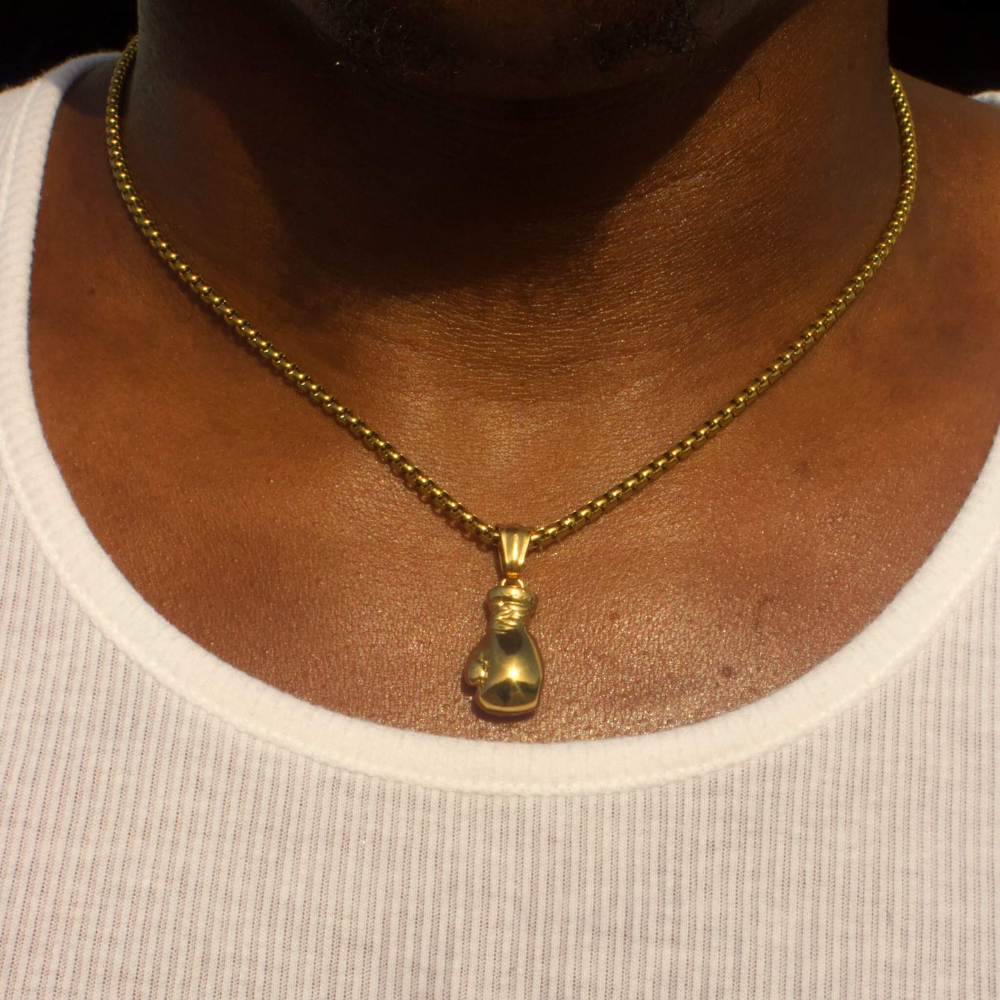 Gold plated boxing glove pendant on a 14k gold plated box chain necklace worn on a person’s neck