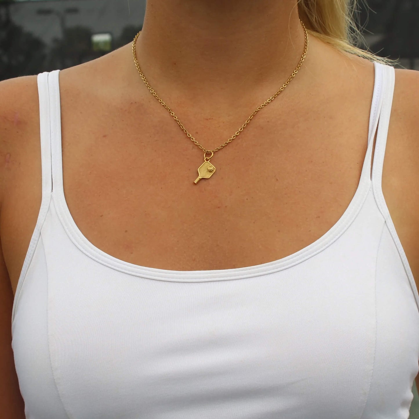 Gold plated pickleball paddle pendant necklace on woman's neck with white tank top