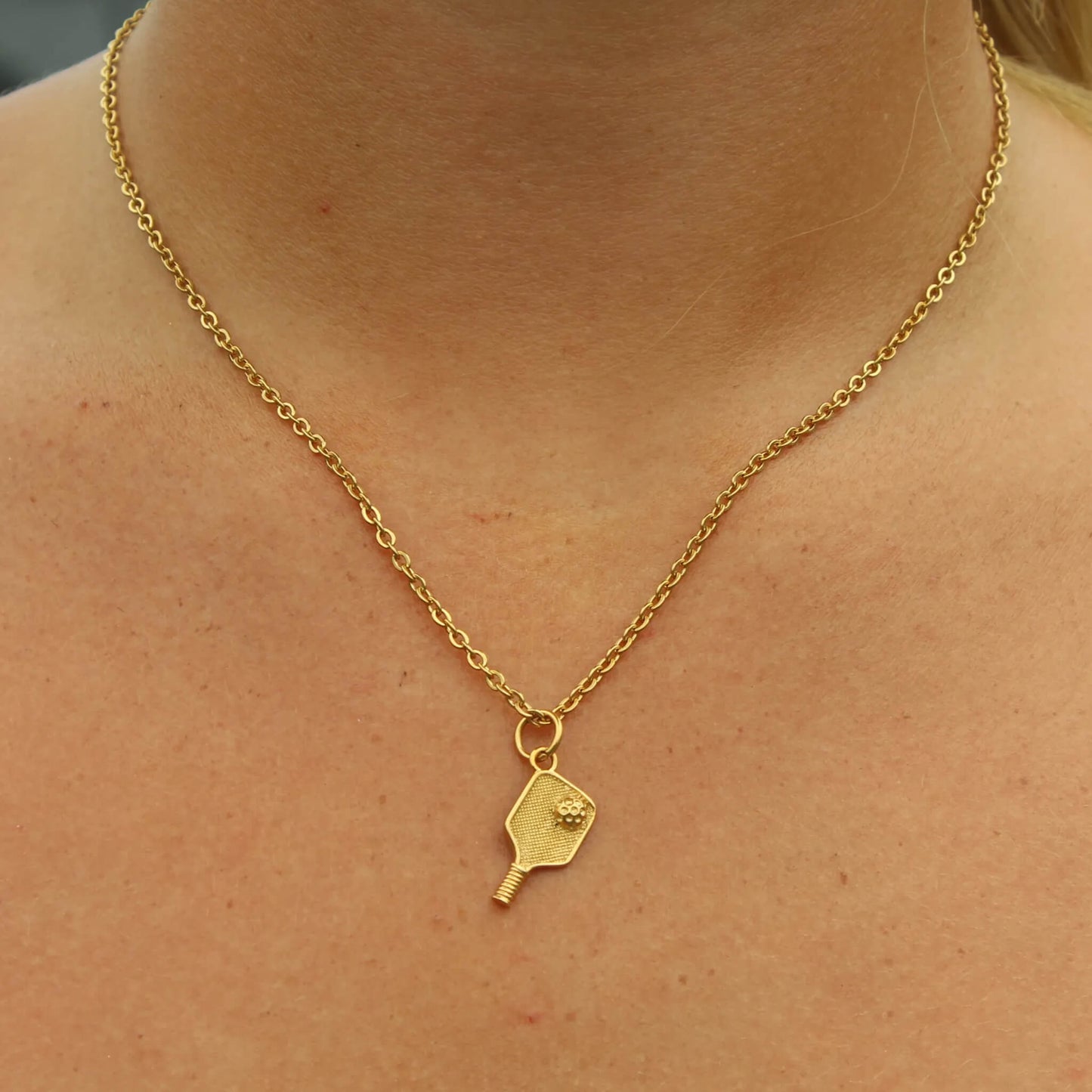 Gold plated pickleball paddle pendant on a delicate chain necklace worn around the neck