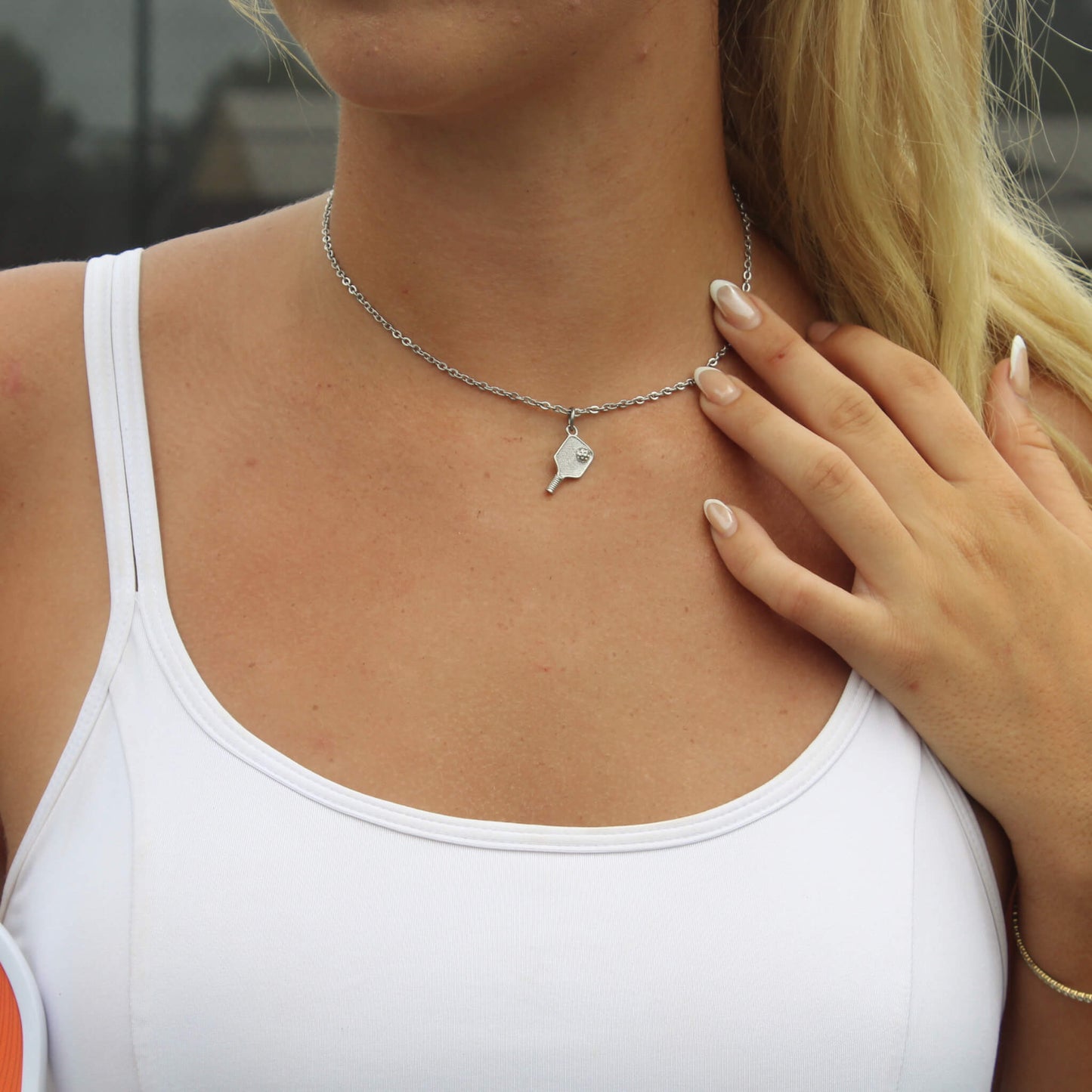 Silver pickleball paddle pendant necklace worn by woman in white tank top