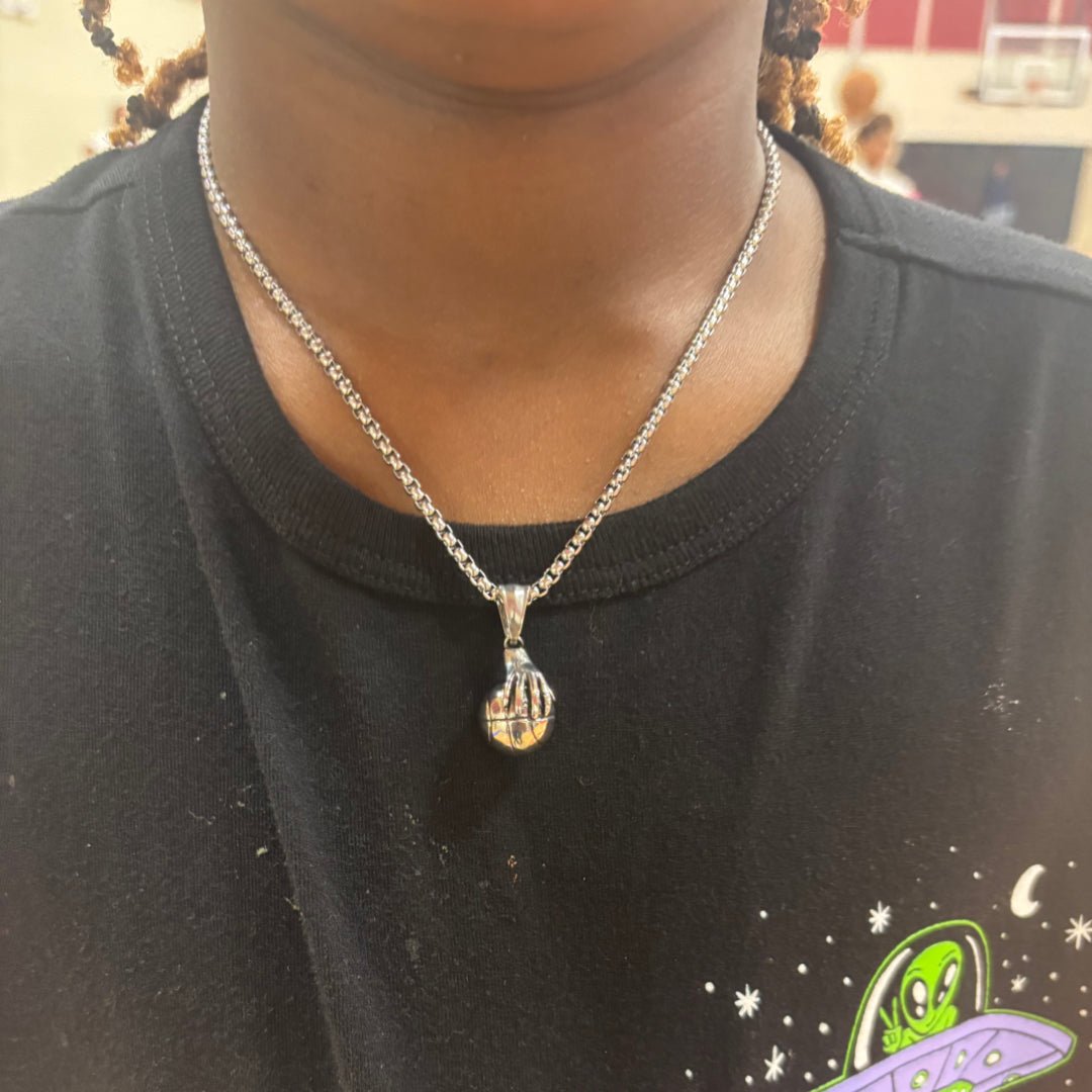 Hand palming basketball pendant on silver chain necklace worn around neck
