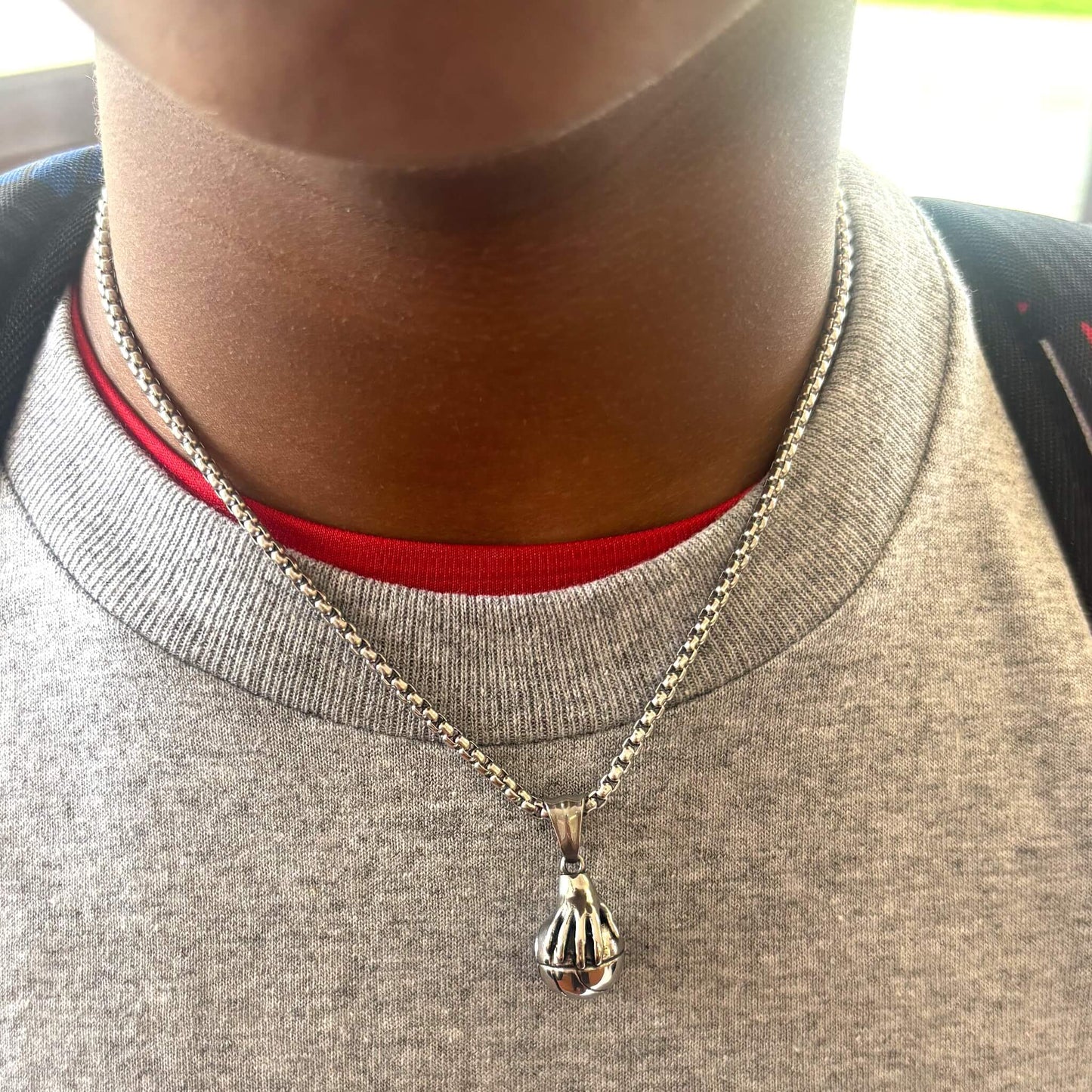 Close-up of a hand palming basketball pendant on a silver chain necklace worn over a grey shirt