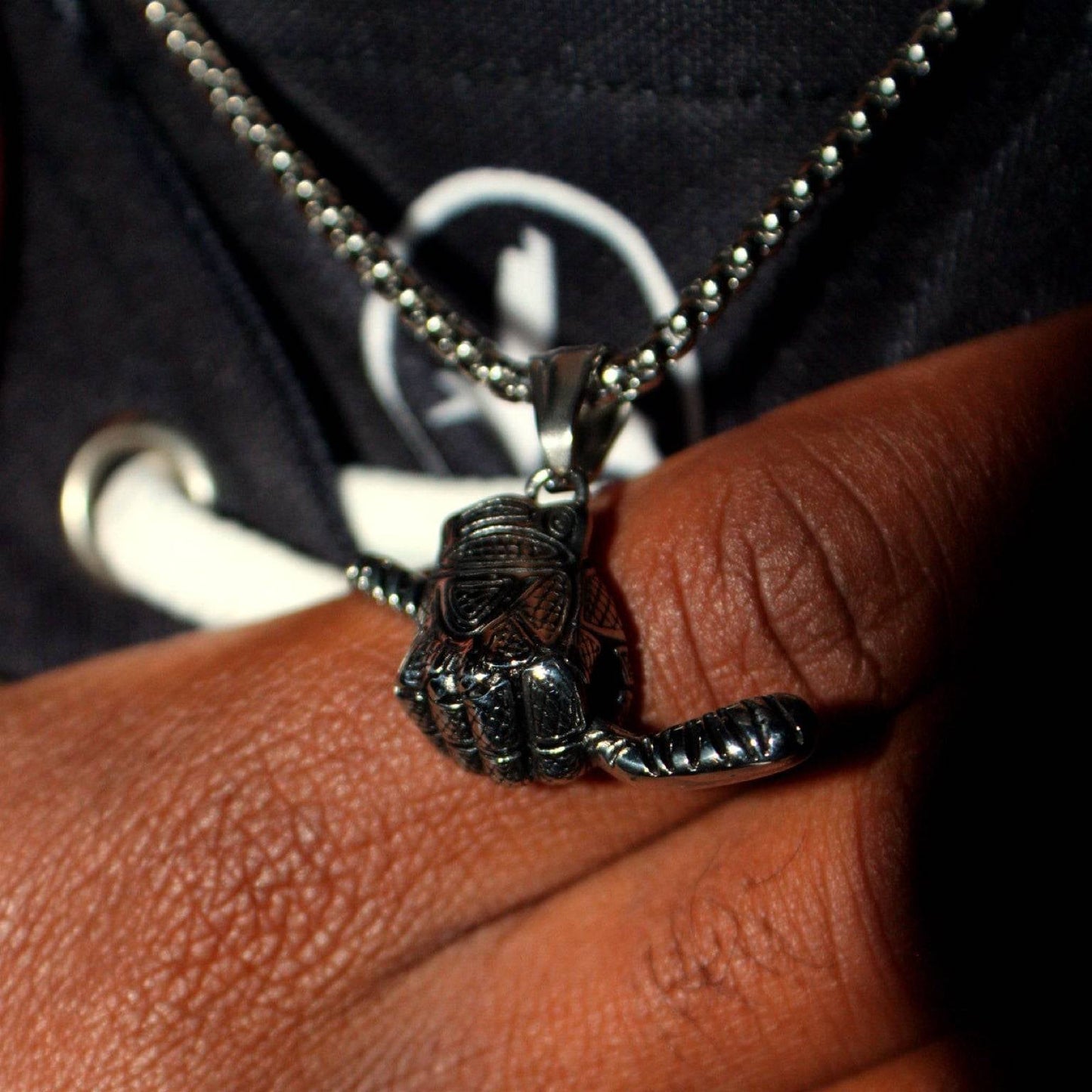 Close-up of a silver hockey glove and stick pendant on a 3mm box chain necklace worn on a wrist.