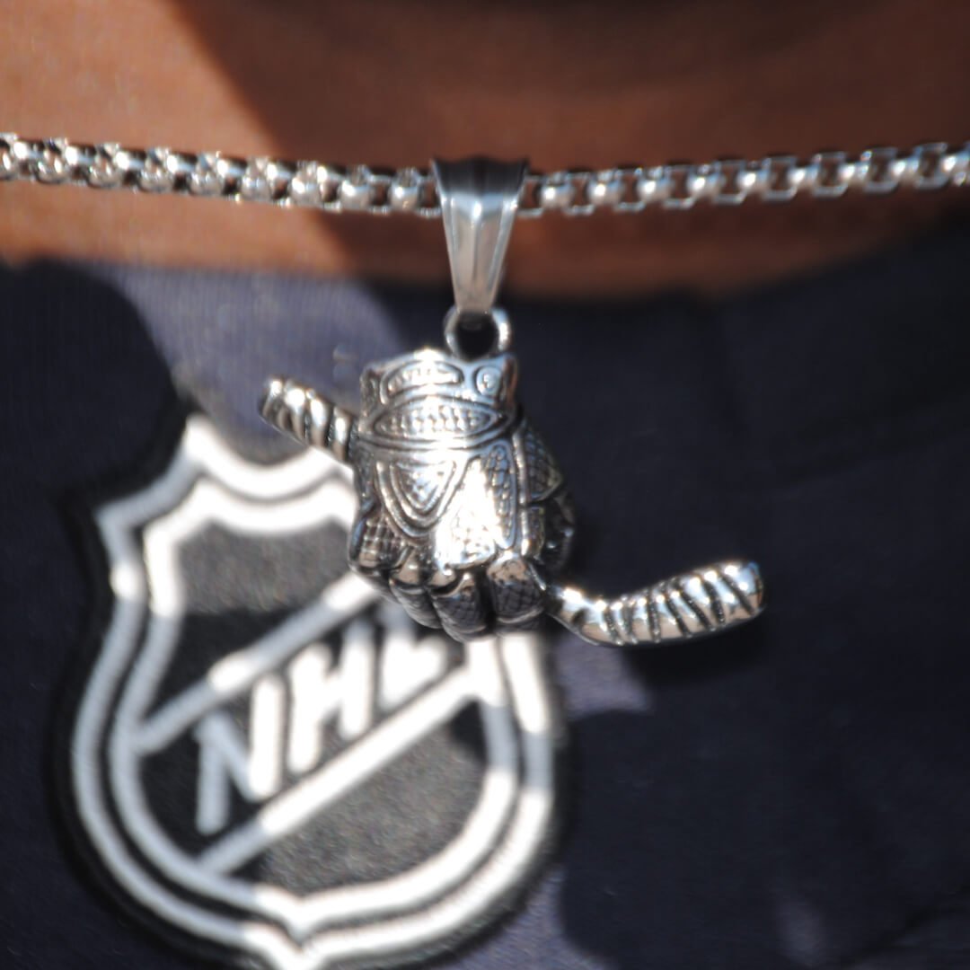 Silver hockey glove and stick pendant necklace on a box chain worn over a dark NHL shirt