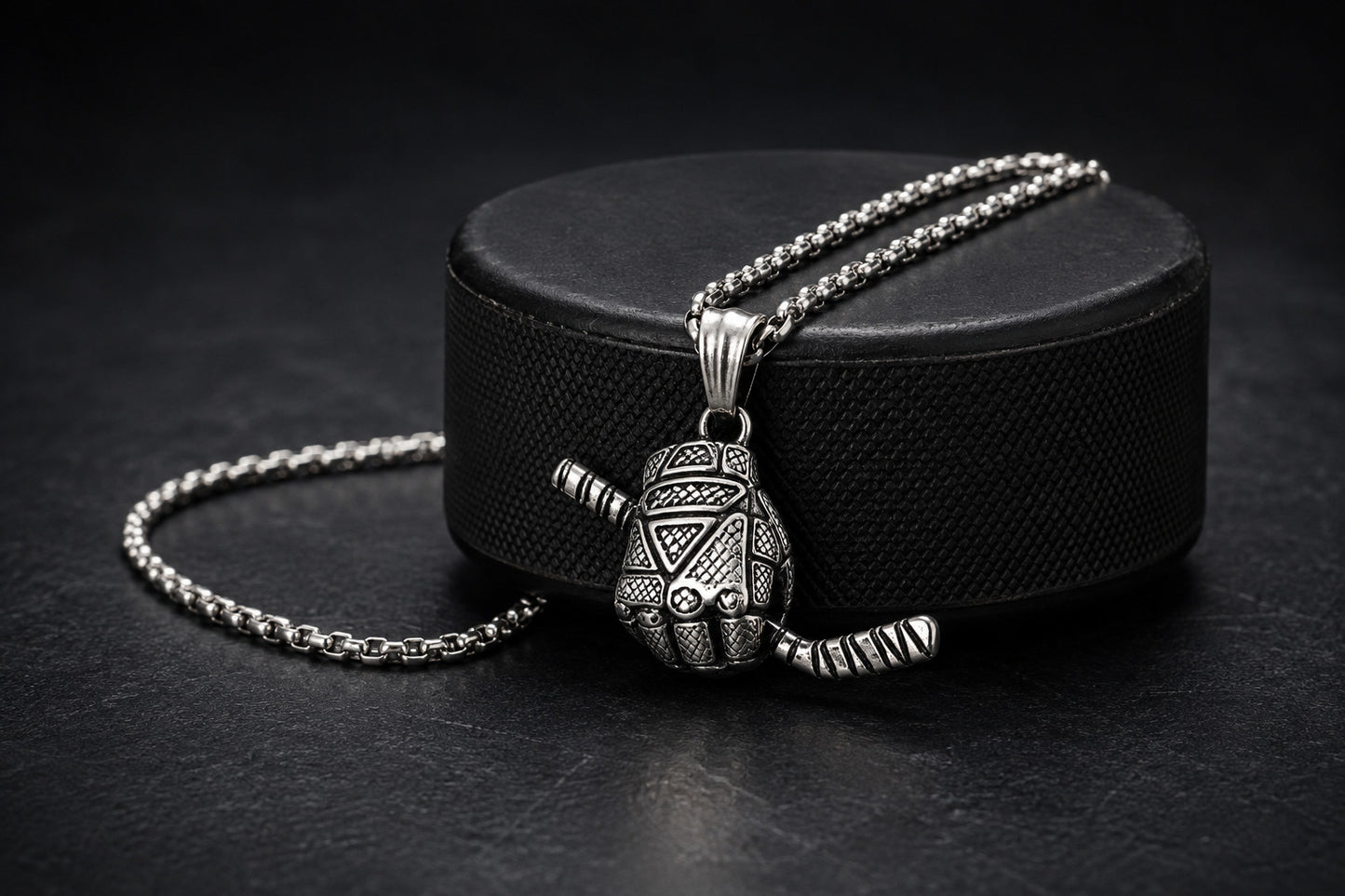 A silver-toned pendant necklace with a detailed hockey glove pendant, displayed on a black hockey puck against a dark background.