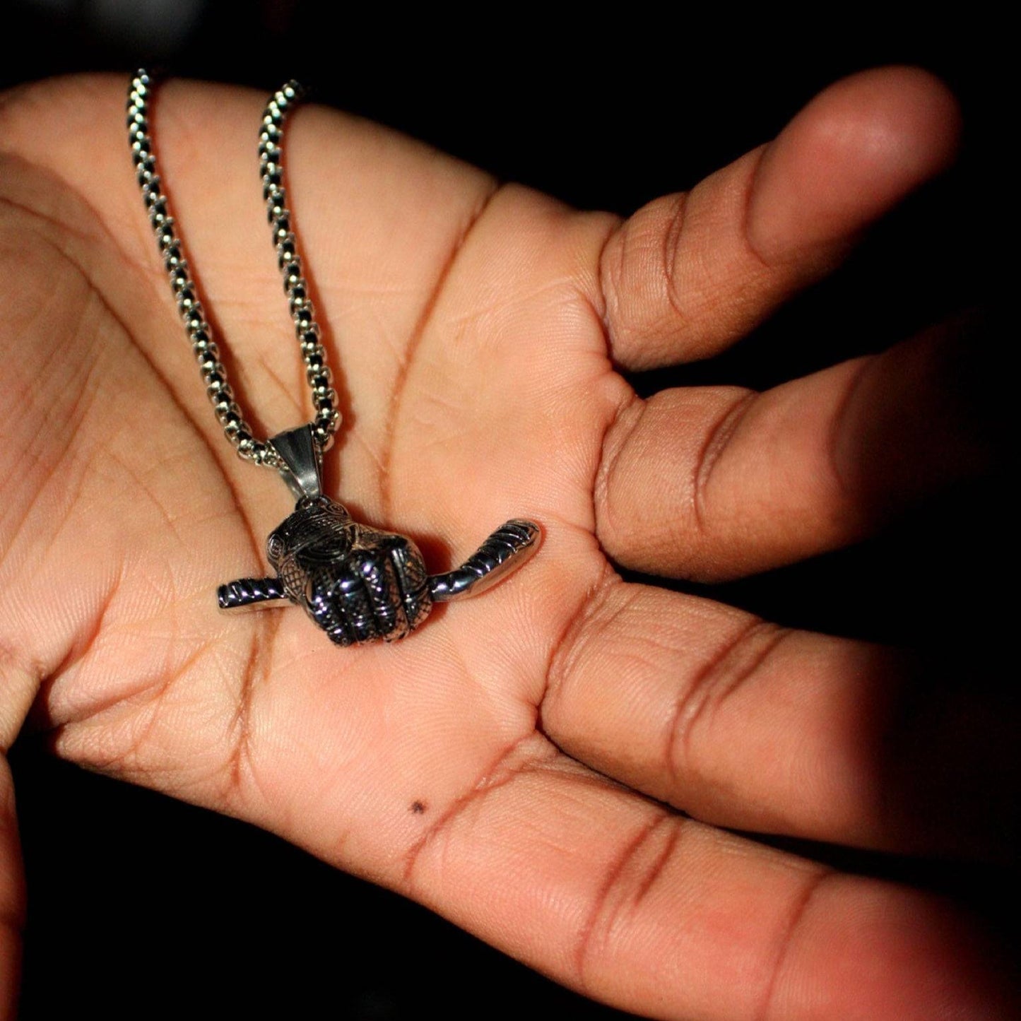 Close-up of a hockey glove and stick pendant necklace held in a hand with a 3mm box chain and lobster clasp in stainless steel