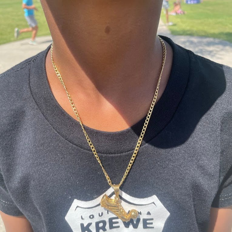 Gold-plated soccer cleat pendant on a 3mm Cuban link chain necklace worn on a person outdoors