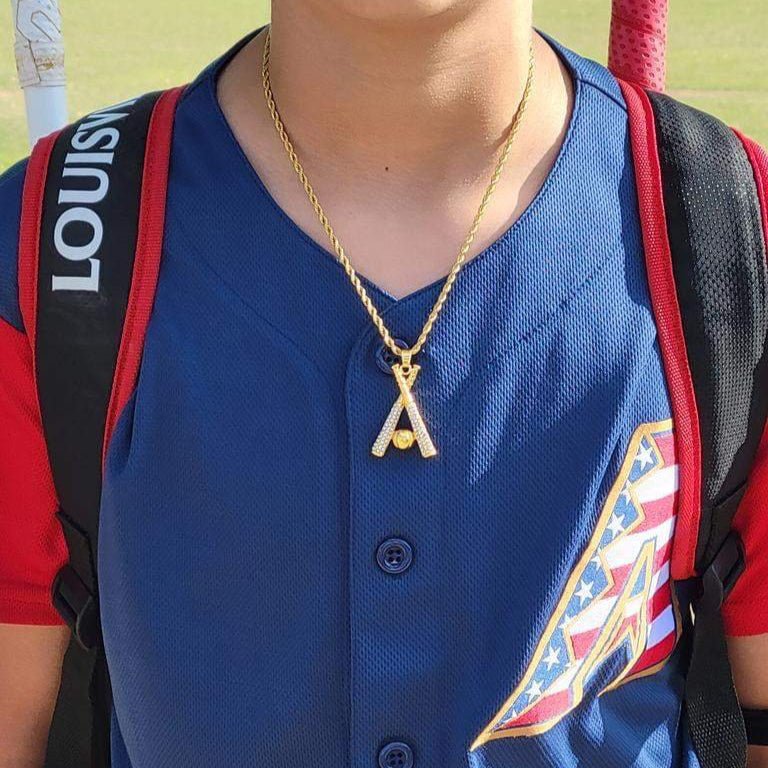 Gold studded baseball bats pendant and chain necklace worn with a blue baseball jersey, symbolizing passion for baseball.