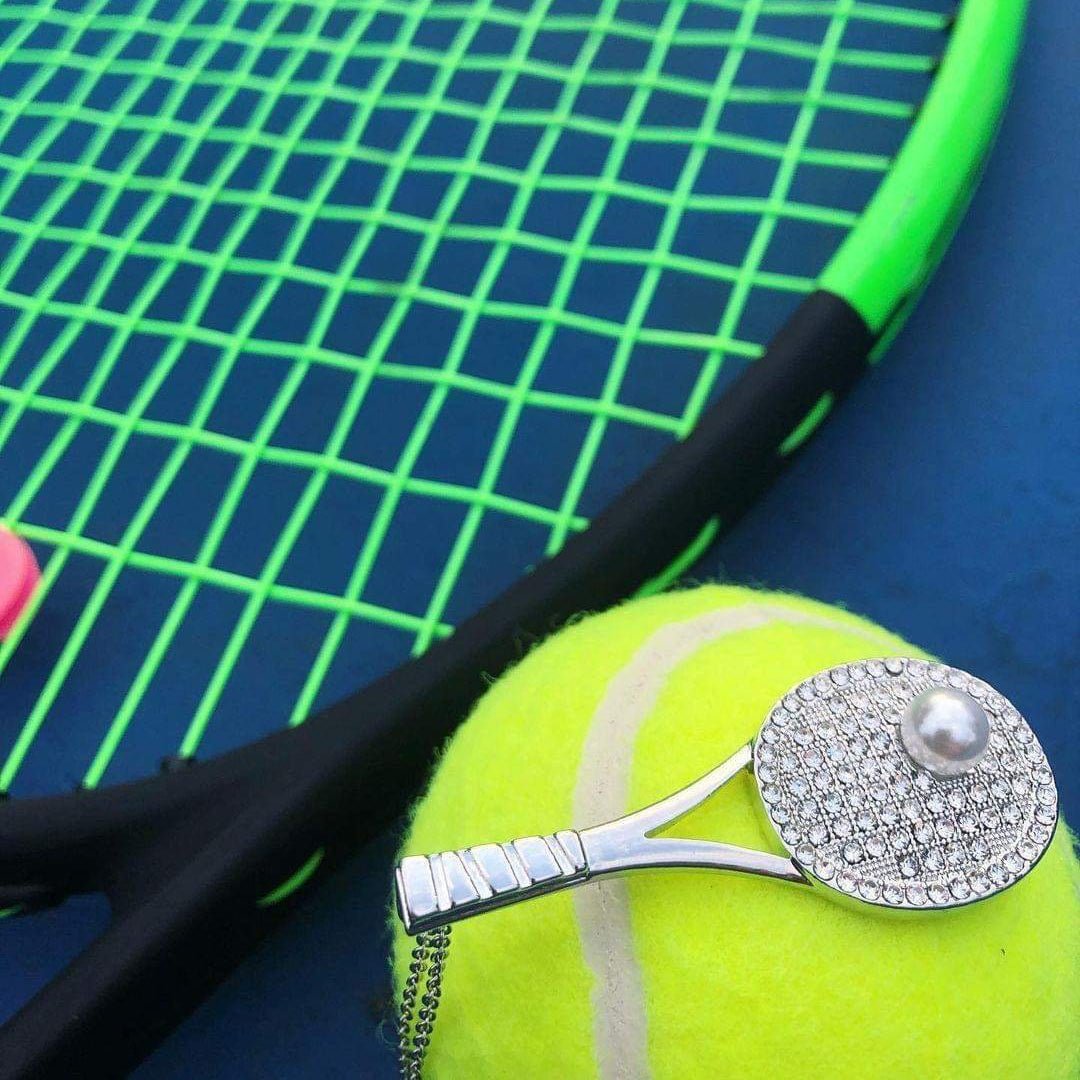 Studded tennis racket pendant necklace with cubic zirconia and pearl detail on tennis ball background