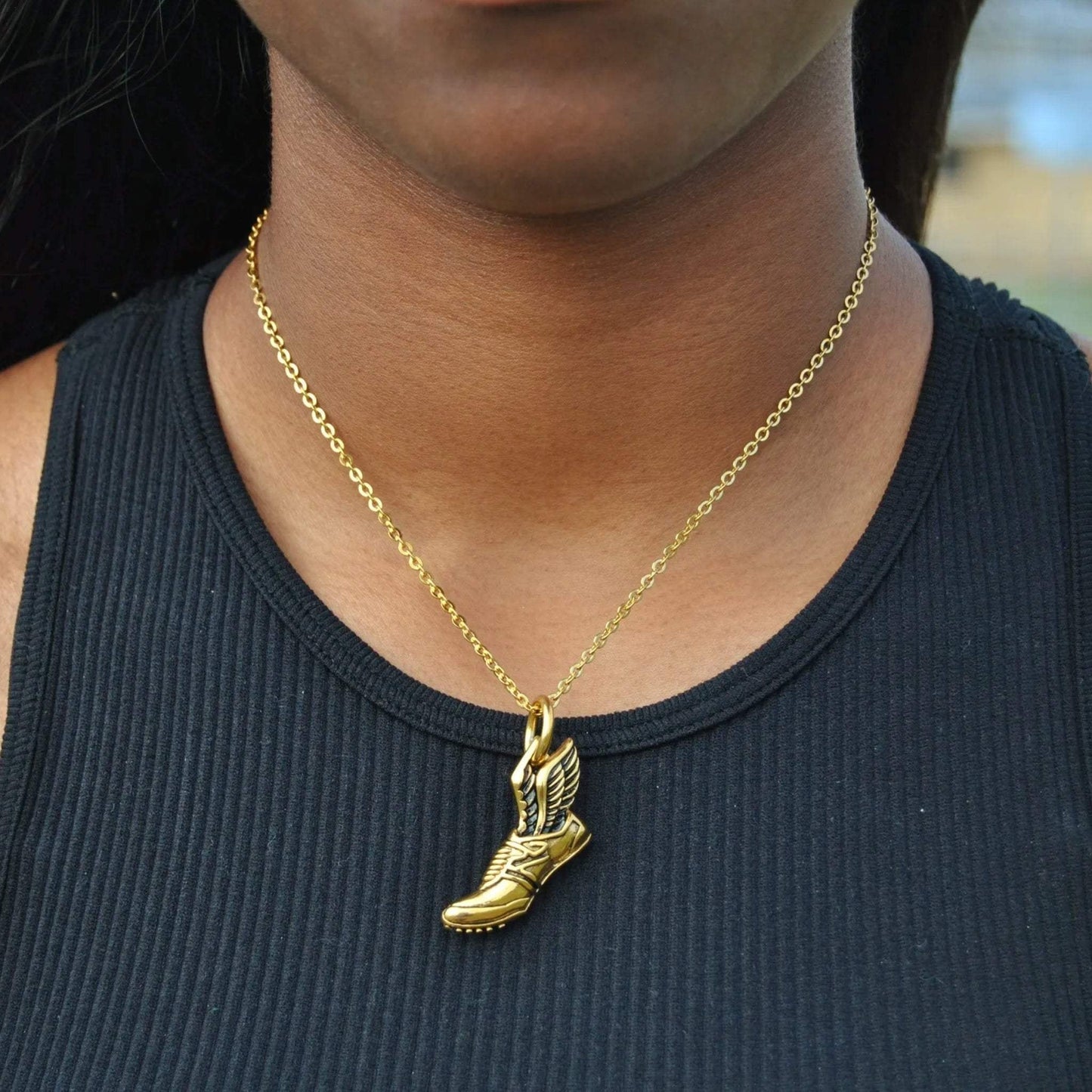 Gold plated winged running shoe pendant on a gold chain necklace worn around the neck