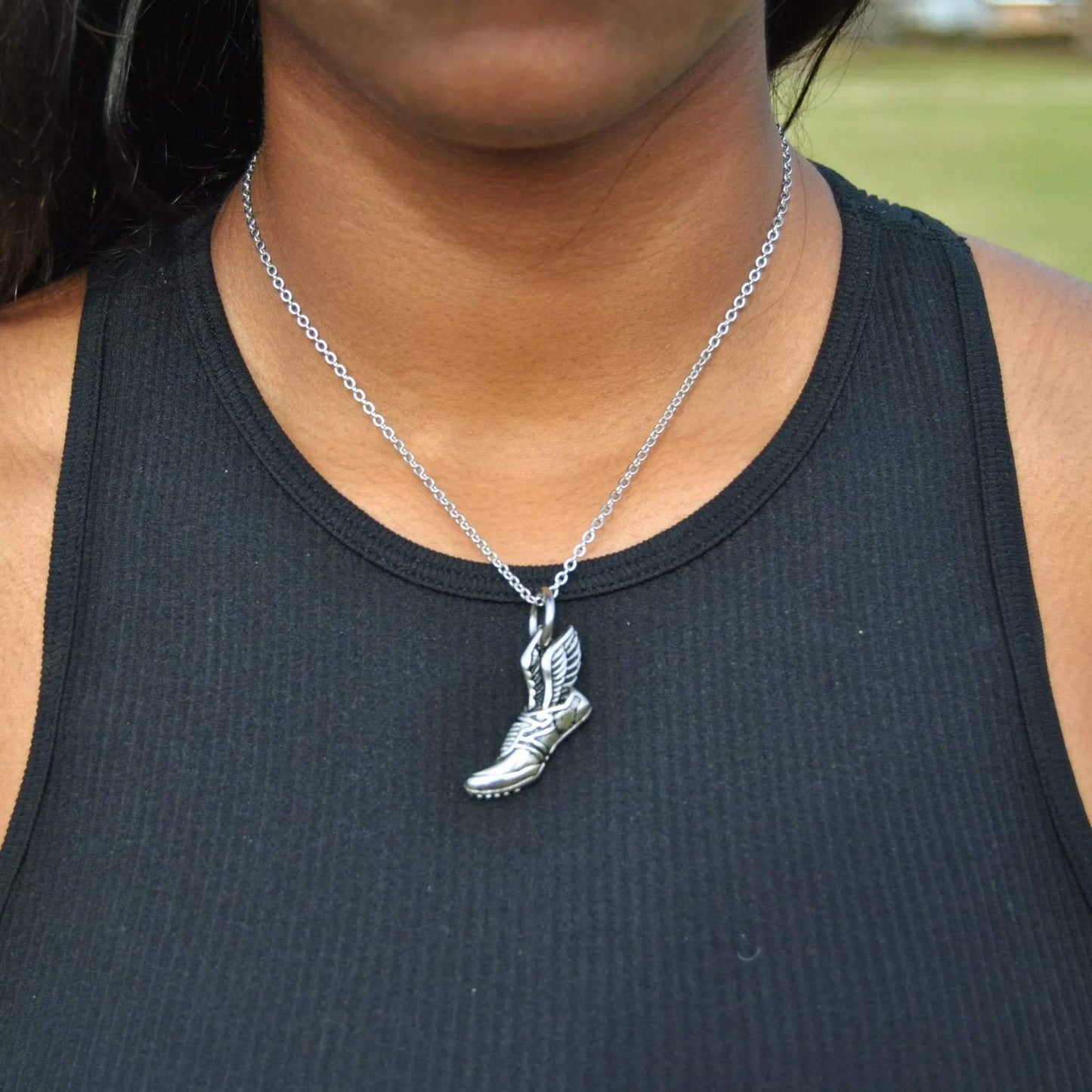 Silver winged running shoe pendant necklace worn on neck with black tank top