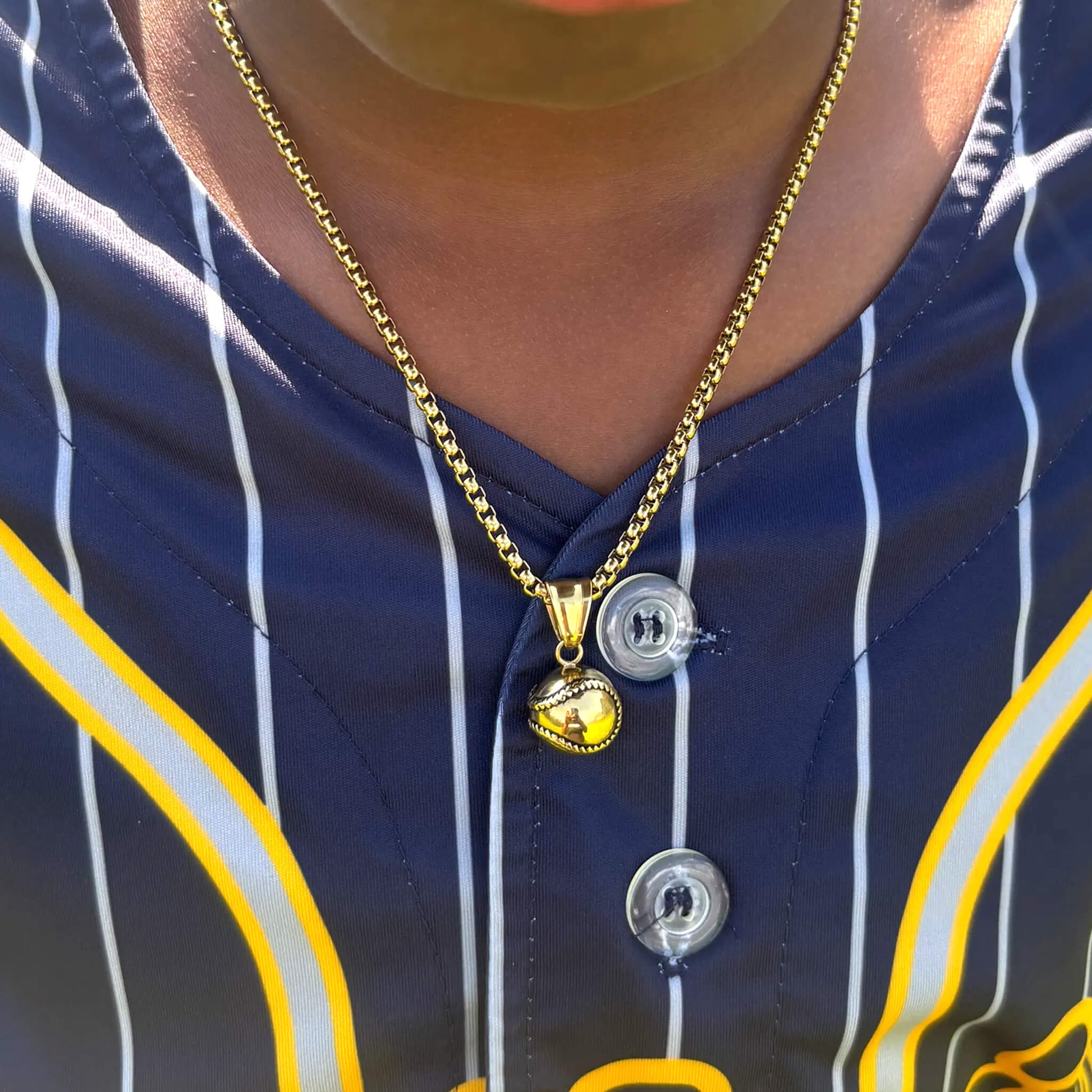 Gold 3D baseball pendant on a gold box chain necklace worn with a navy and yellow sports jersey