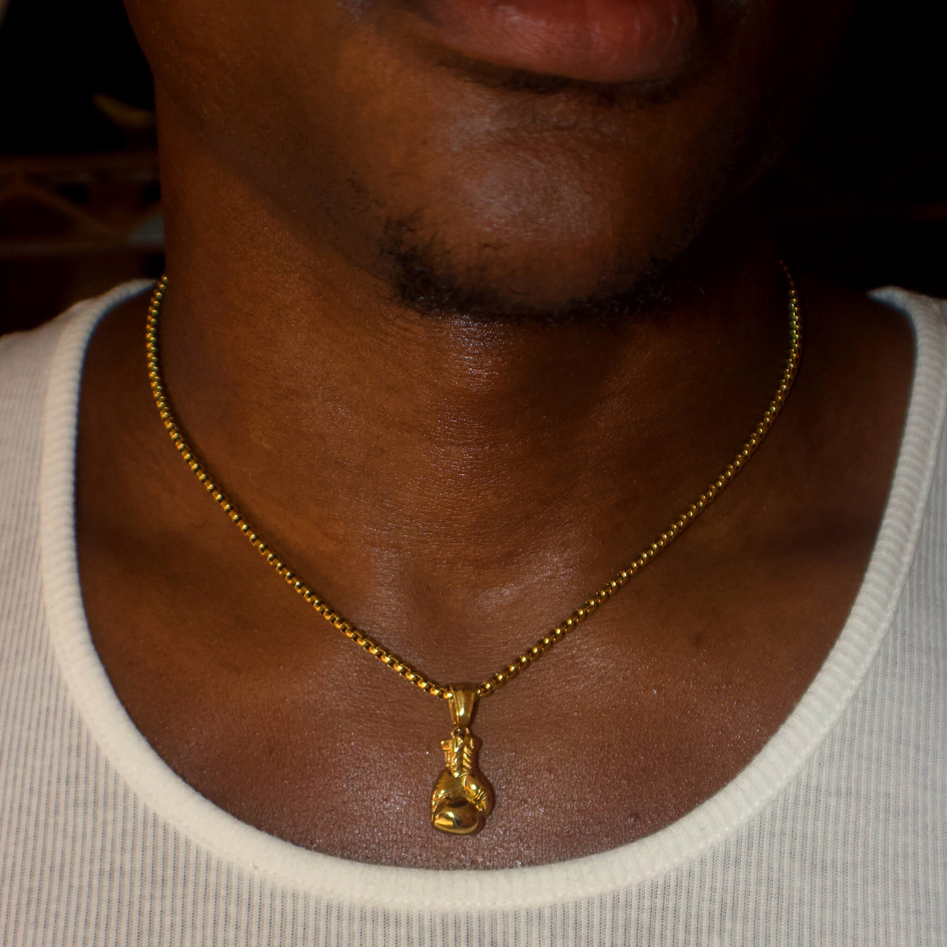 Close-up of a person wearing a gold boxing glove pendant on a 3mm box chain necklace.