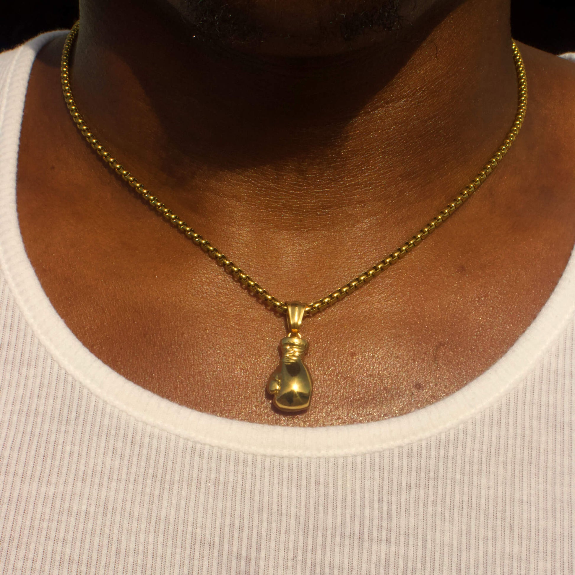 Gold plated boxing glove pendant on a 14k gold plated box chain necklace worn on a person’s neck