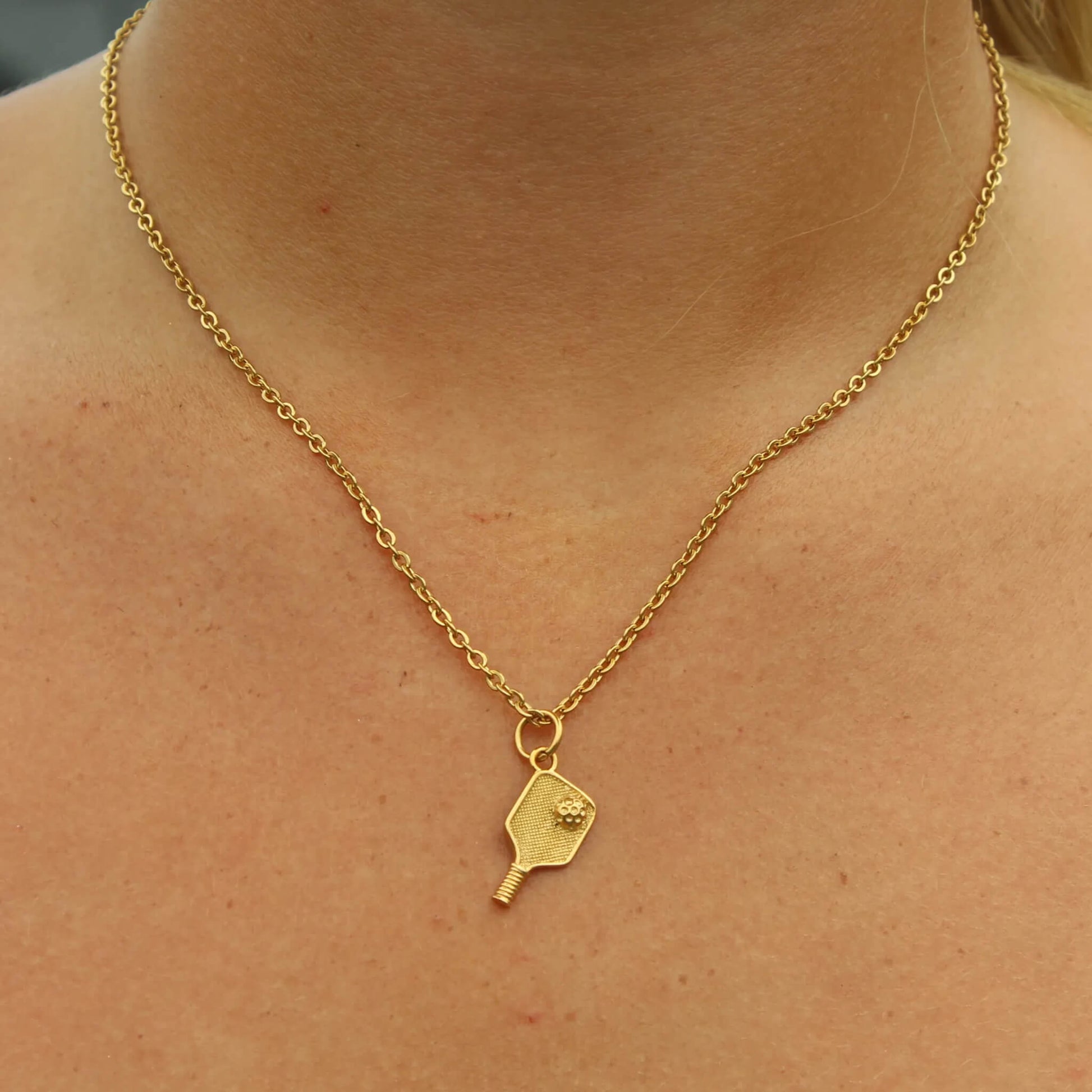 Gold plated pickleball paddle pendant on a delicate chain necklace worn around the neck