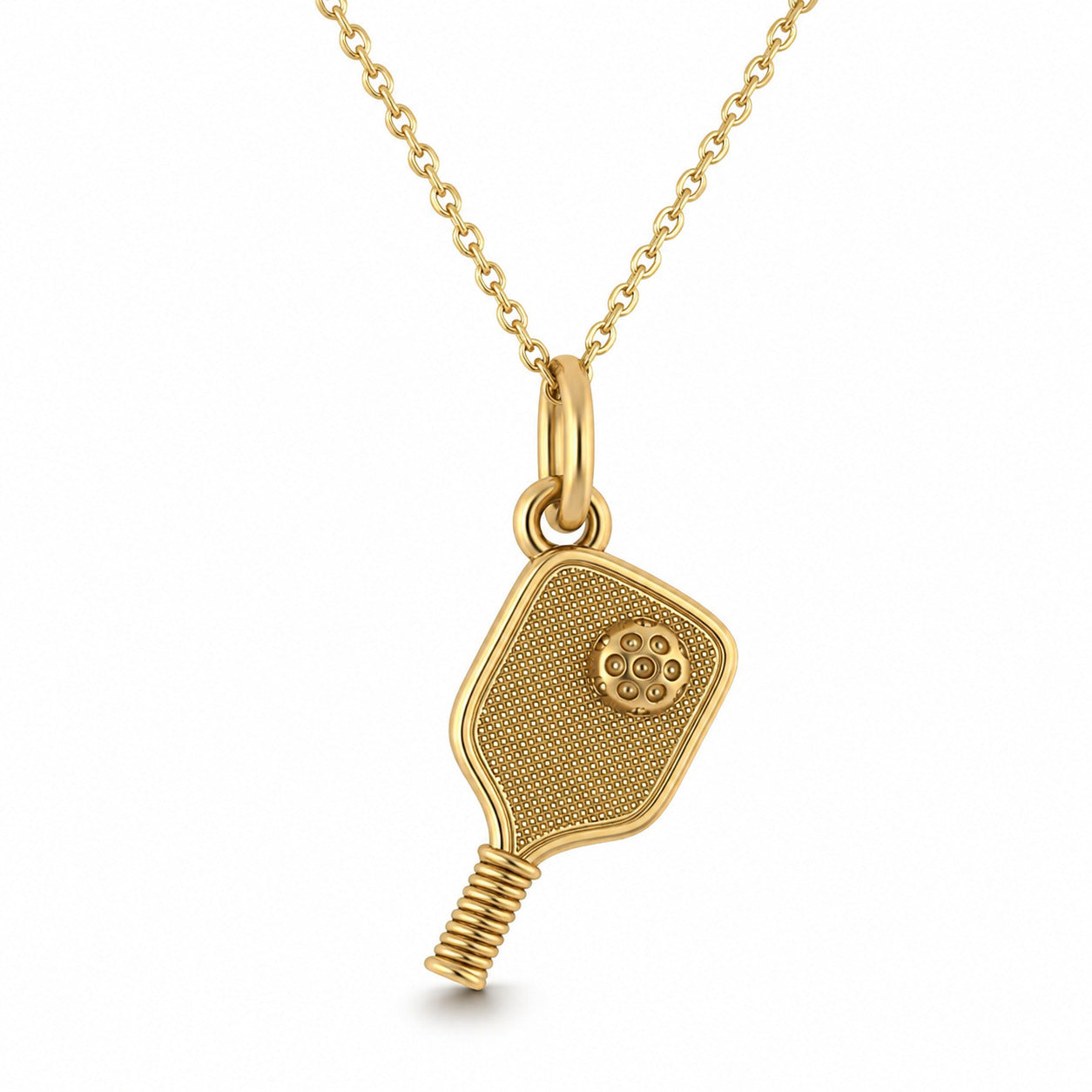 A gold pendant necklace featuring a pickleball paddle design with a textured face, a small floral emblem, and a wrapped handle, suspended from a delicate gold chain on a white background. 
