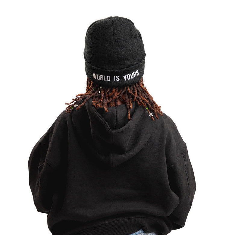 A person shown from behind wearing a black oversized hoodie, a black beanie with white text reading 'WORLD IS YOURS', and blue jeans against a plain white background.