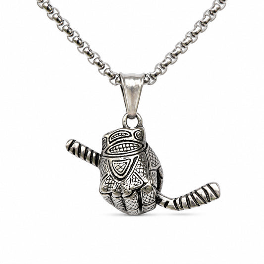 A silver-toned pendant necklace featuring a stylized hand holding a hockey stick, detailed with engraved patterns, suspended from a matching box chain against a plain white background.