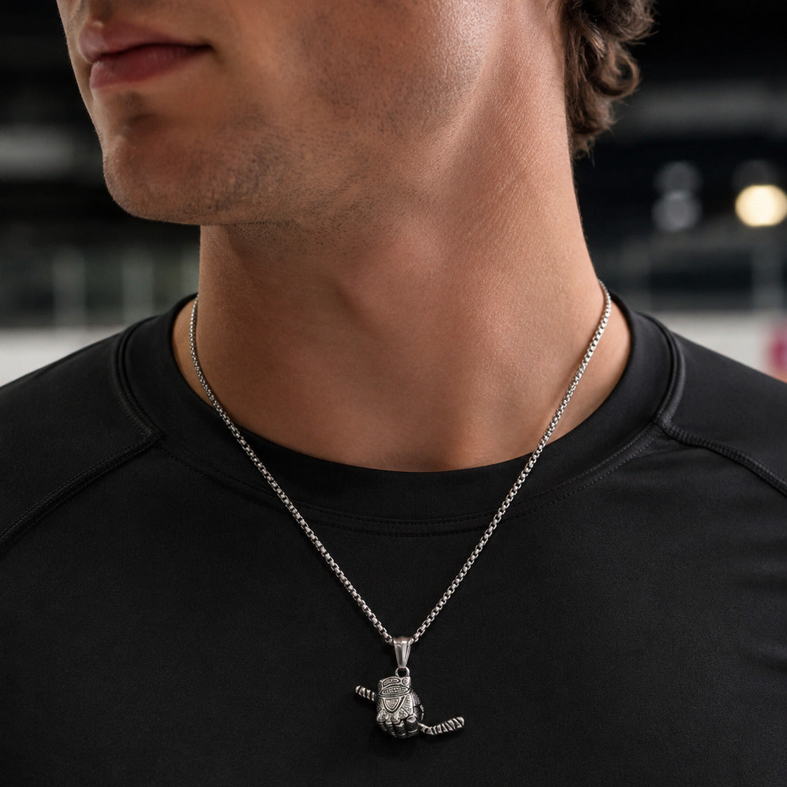 A close-up of a man wearing a silver pendant necklace with a hockey glove holding a hockey stick over a black athletic shirt.